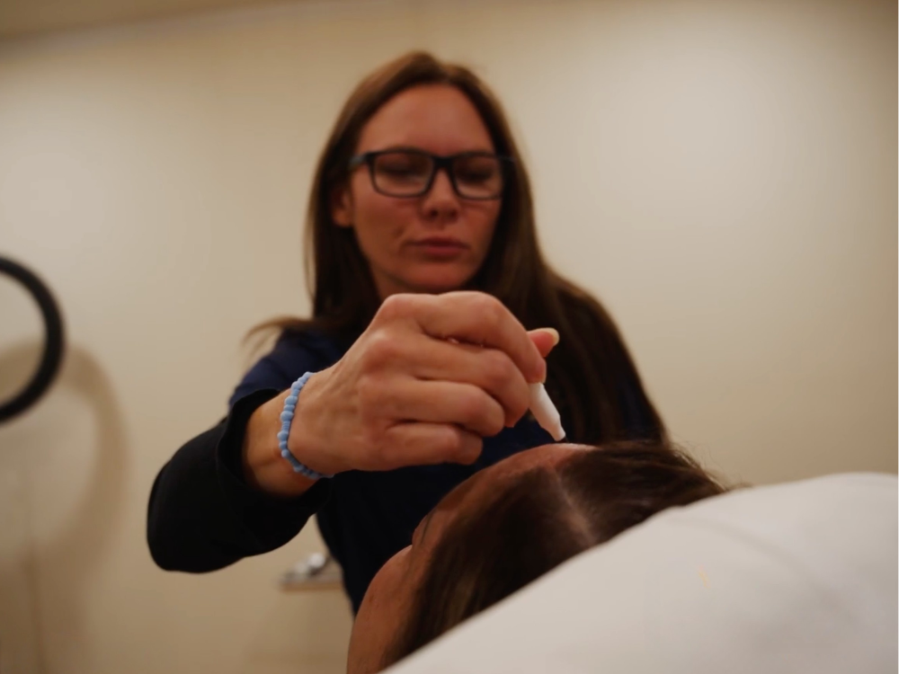 Medical practitioner applying a dropper to a patient's scalp during a treatment.
